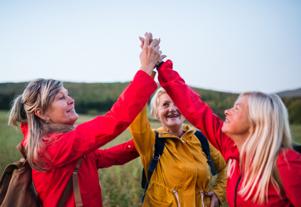 Senior women friends on walk outdoors in nature at dusk, giving high five.