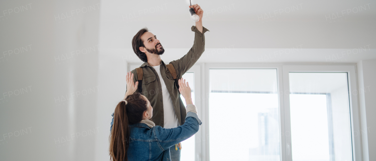 A young couple changing light bulb in new flat, moving, new home and relocation concept.