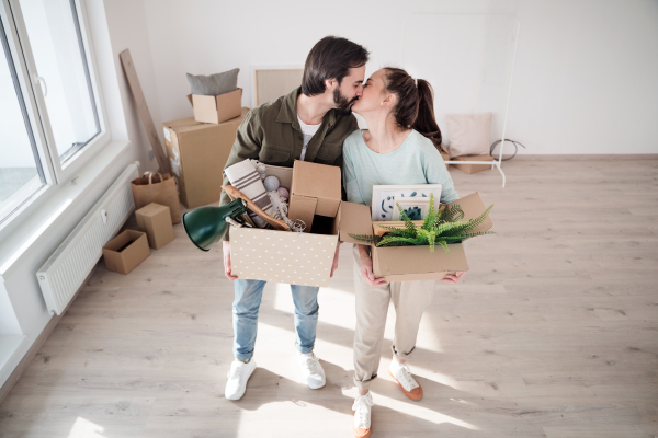 Happy young couple with boxes kissing when moving in new flat, new home and relocation concept.