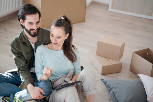 A young couple with tablet planning when moving in new flat, new home and relocation concept.