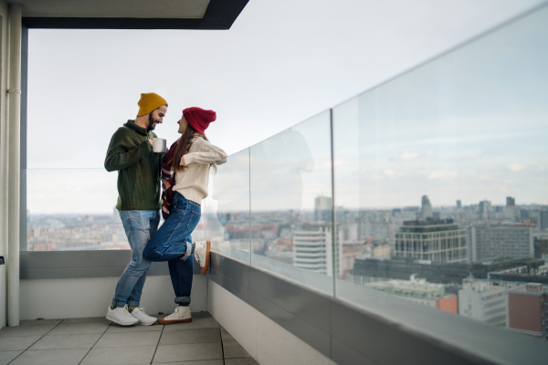 Happy young couple owners with coffee on balcony in new flat, moving in, new home and relocation concept.