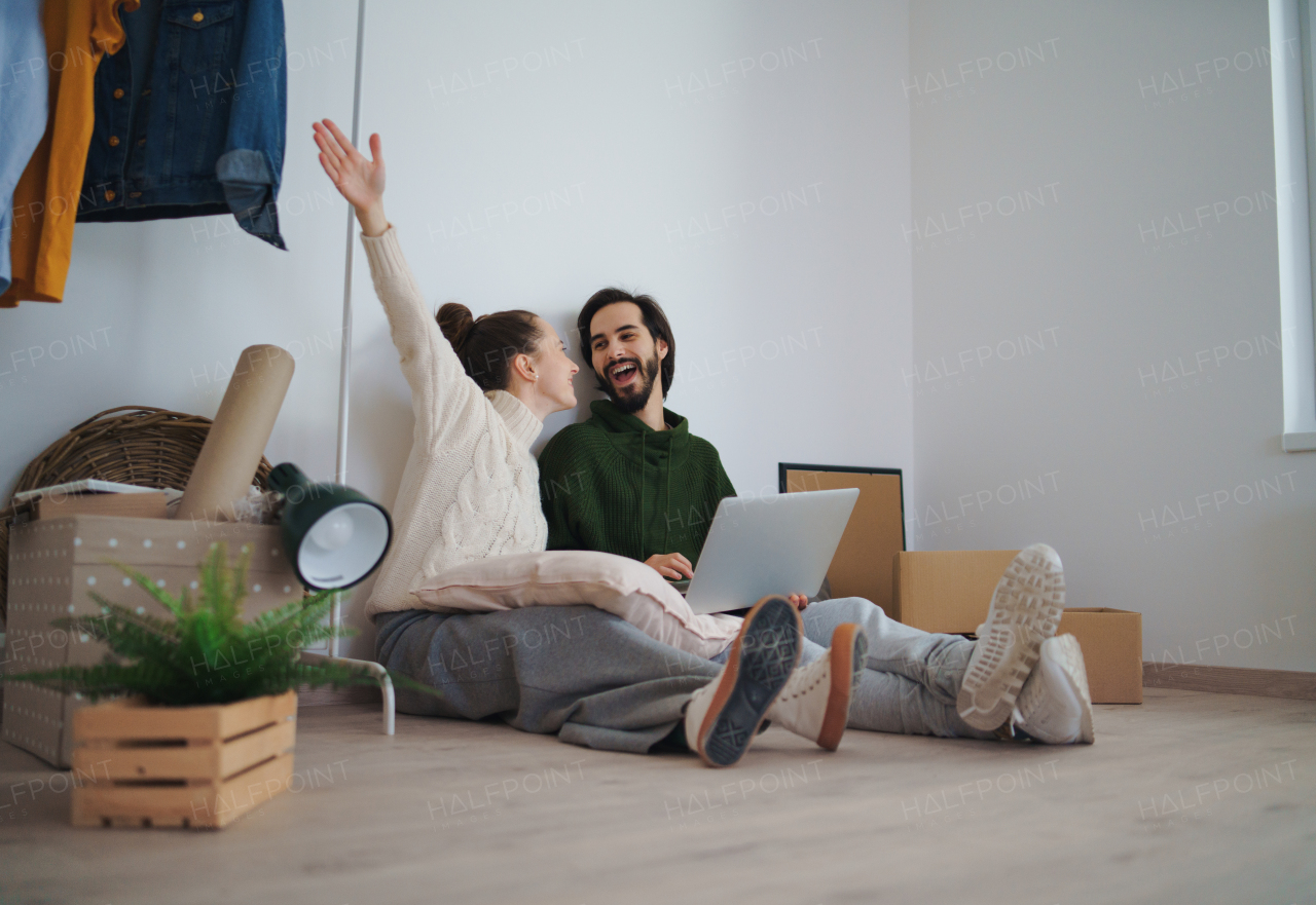 A young couple with laptop sitting on floor and planning when moving in new flat.