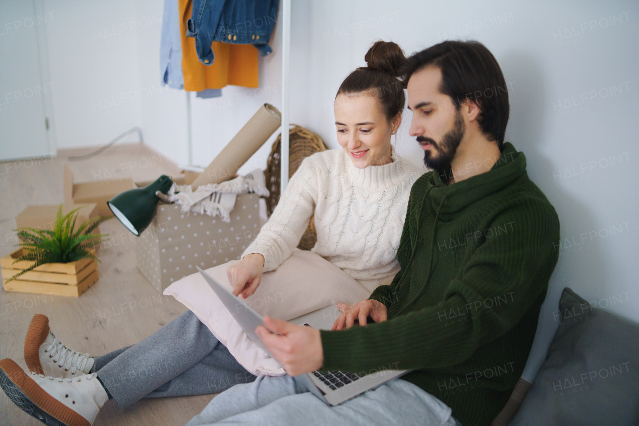 Happy young couple with laptop and boxes moving in new flat, new home and relocation concept.