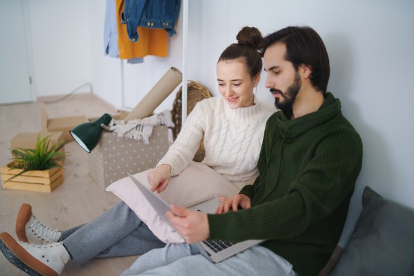 Happy young couple with laptop and boxes moving in new flat, new home and relocation concept.