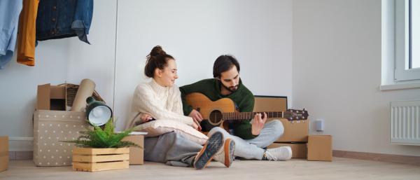 Happy young couple with boxes and guitar moving in new flat, new home and relocation concept.