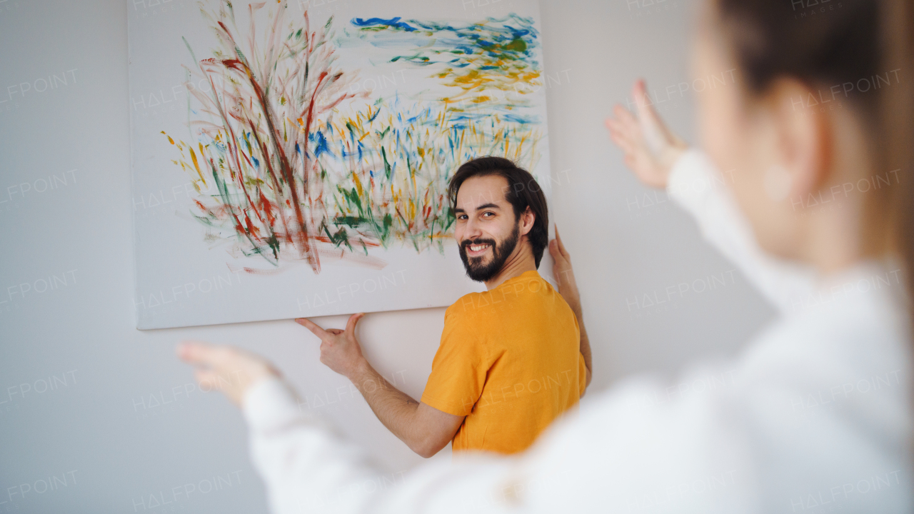 A young couple arranging new flat, hanging up painting, new home and relocation concept.