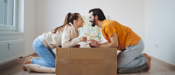 Happy young couple with boxes and wine moving in new flat, new home and relocation concept.