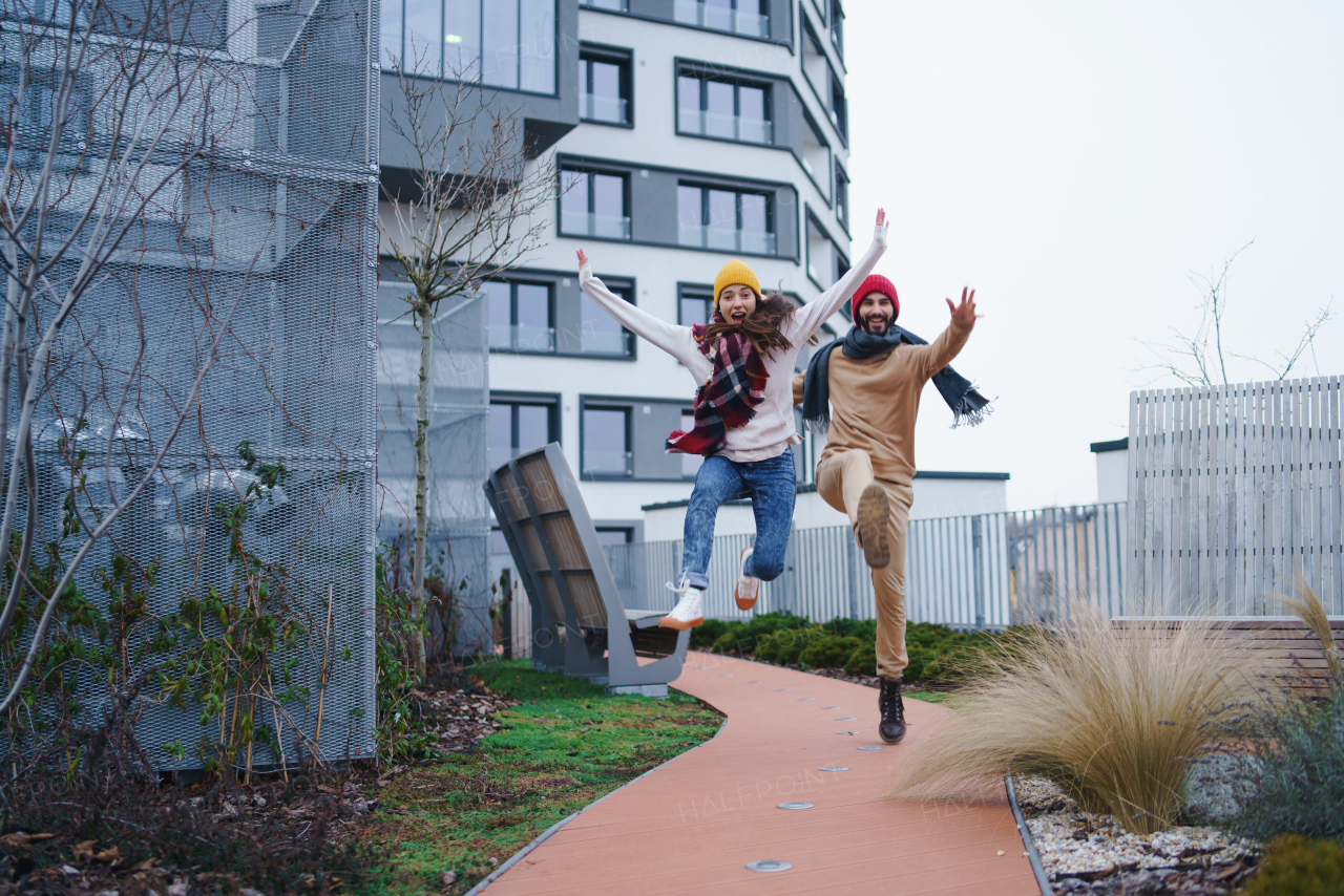 A cheerful young couple owners jumping outdoors in front of new flat, new home and relocation concept.