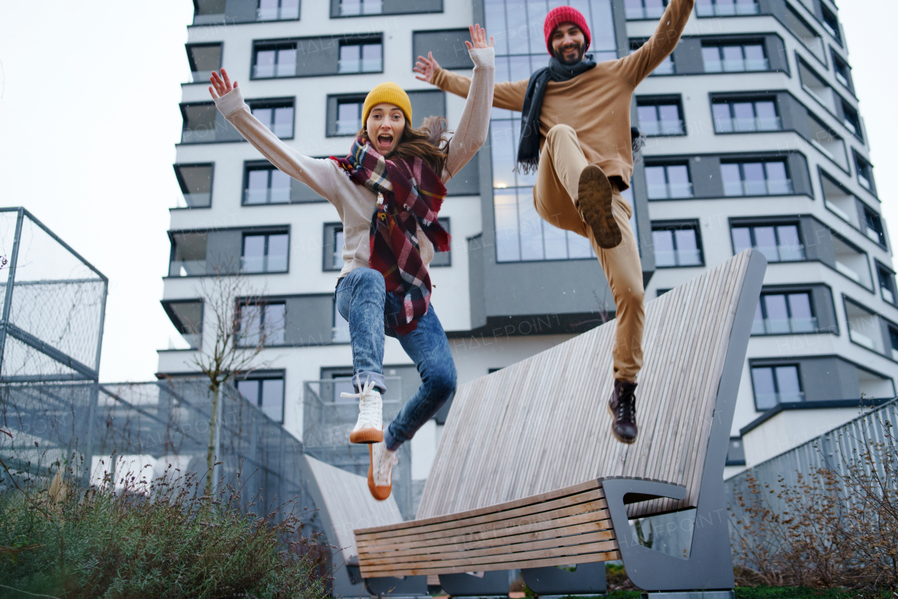 Low angle of cheerful young couple owners jumping outdoors in front of new flat, new home and relocation concept.