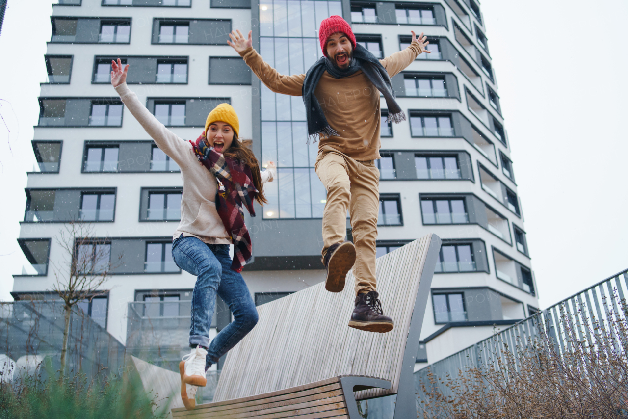 Low angle of cheerful young couple owners jumping outdoors in front of new flat, new home and relocation concept.