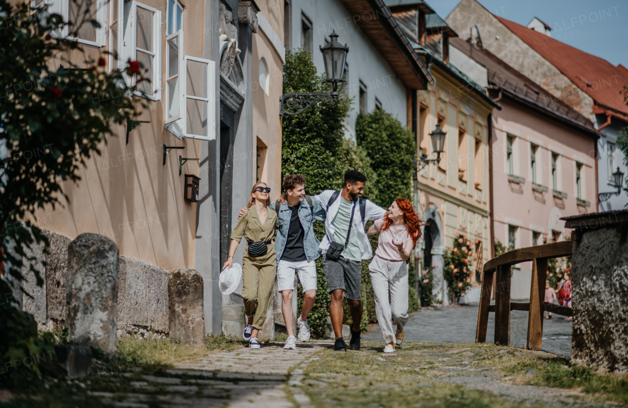 A front view of group of happy young people outdoors on trip in town, walking and talking.