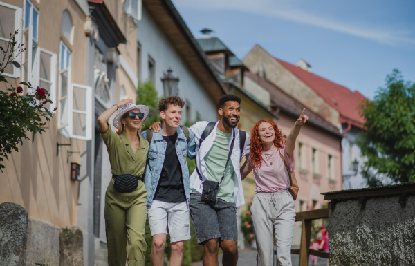 A front view of group of happy young people outdoors on trip in town, walking arm in arm.