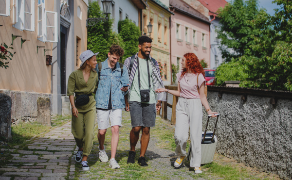 A front view of group of happy young people outdoors on trip in town, walking and talking.