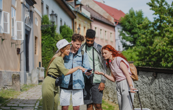 Portrait of group of young people outdoors on trip in town, using online map on smartphone.