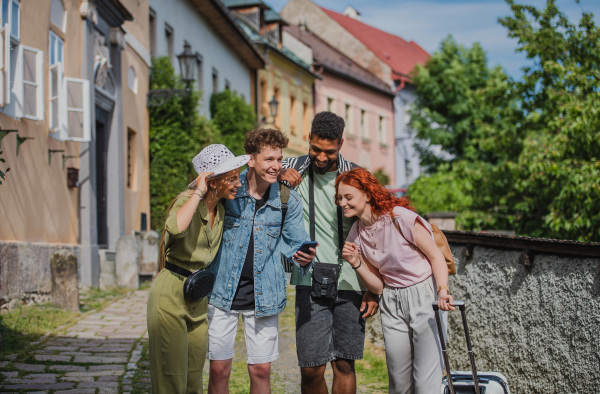 Portrait of group of young people outdoors on trip in town, using online map on smartphone.