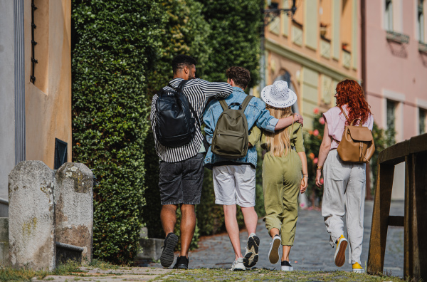 A rear view of group of happy young people outdoors on trip in town, walking arm in arm.