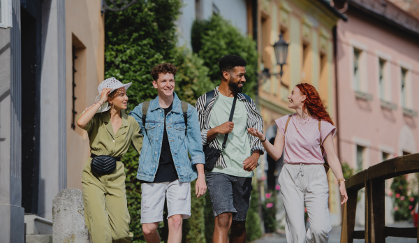 A front view of group of happy young people outdoors on trip in town, walking and talking.