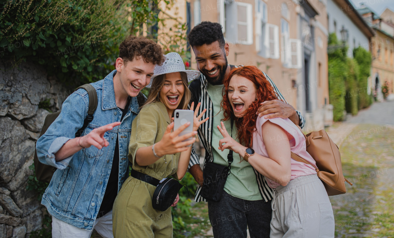 A portrait of group of young people outdoors on trip in town, taking selfie with smartphone.