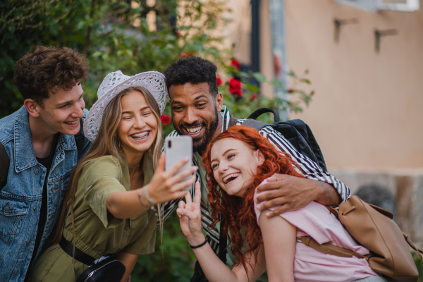 A portrait of group of young people outdoors on trip in town, taking selfie with smartphone.