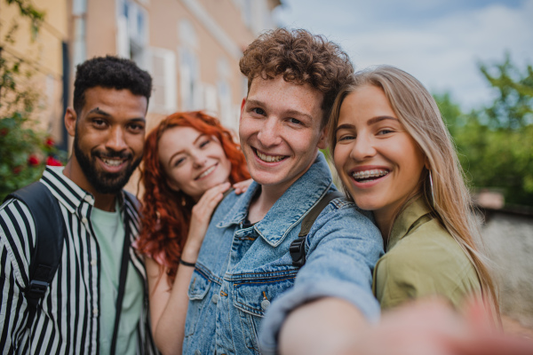 A portrait of group of young people outdoors on trip in town, taking selfie and looking at camera.