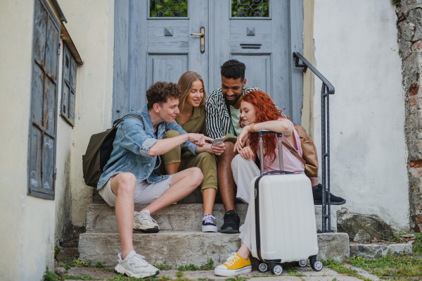 Portrait of group of young people outdoors on trip in town, using online map on smartphone.