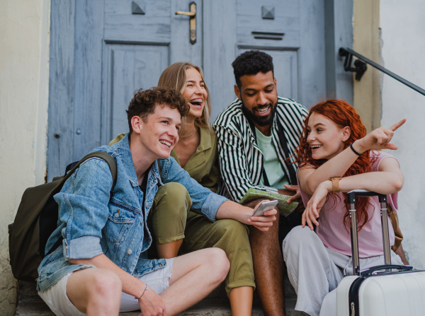 Portrait of group of young people outdoors on trip in town, resting on stairs and talking.