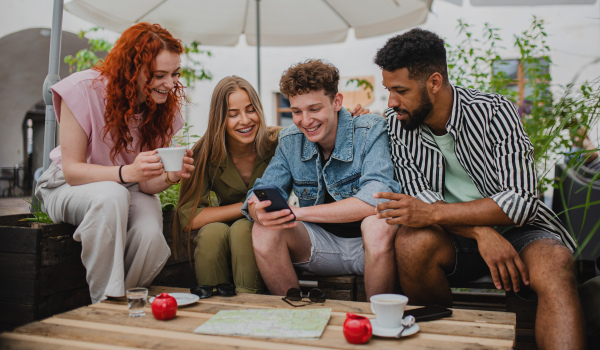 A group of happy young people with smartphone sitting in outdoors cafe on town trip, talking.