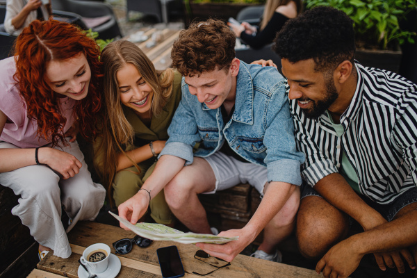 A top view of group of happy young people sitting in outdoors cafe on town trip, using map.