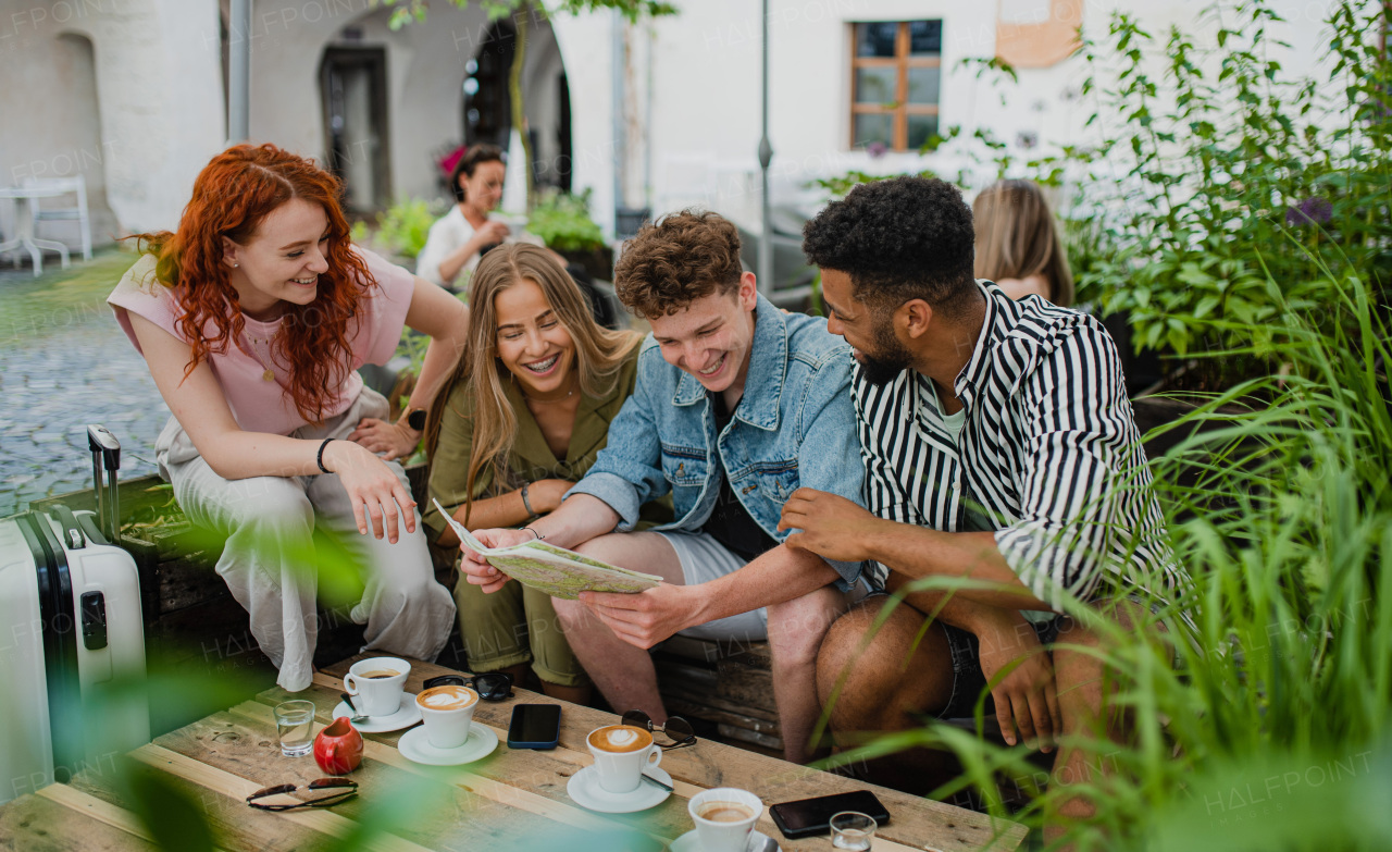 A group of happy young people sitting in outdoors cafe on town trip, using map.