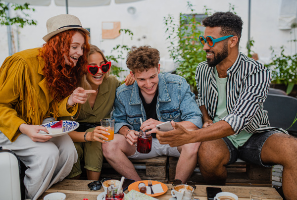 A group of happy young people with smartphone sitting in outdoors cafe on town trip, talking.