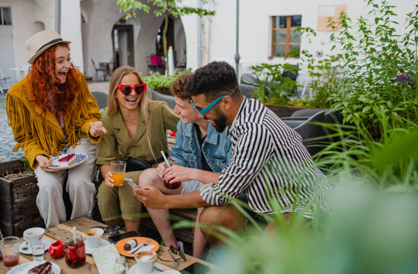 A group of happy young people sitting in outdoors cafe on town trip, talking.