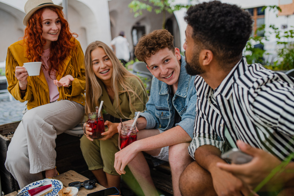 A group of happy young people sitting in outdoors cafe on town trip, talking.