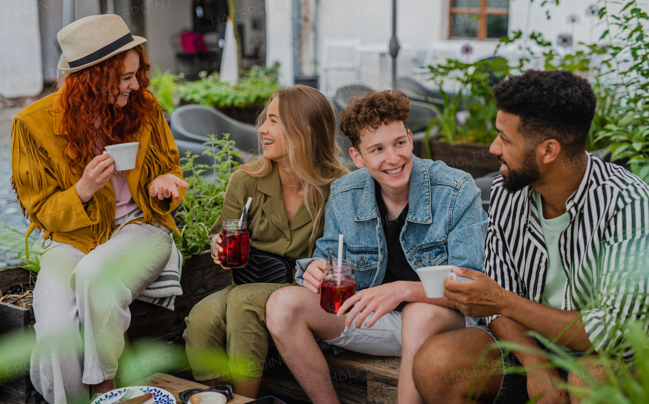 A group of happy young people sitting in outdoors cafe on town trip, talking.