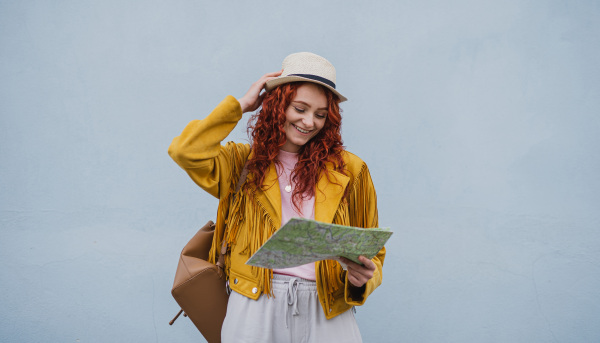 A young woman tourist outdoors against white background on trip in town, using paper map.