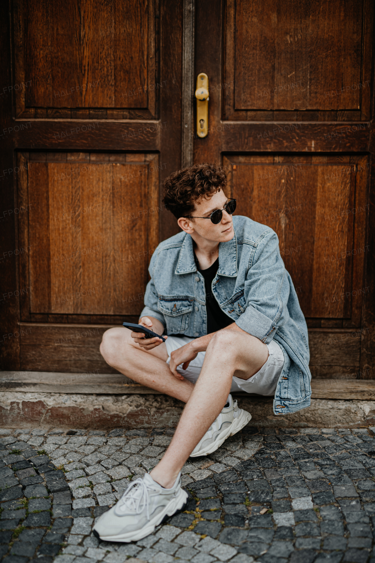 A portrait of happy young man outdoors in front of door, using smartphone.