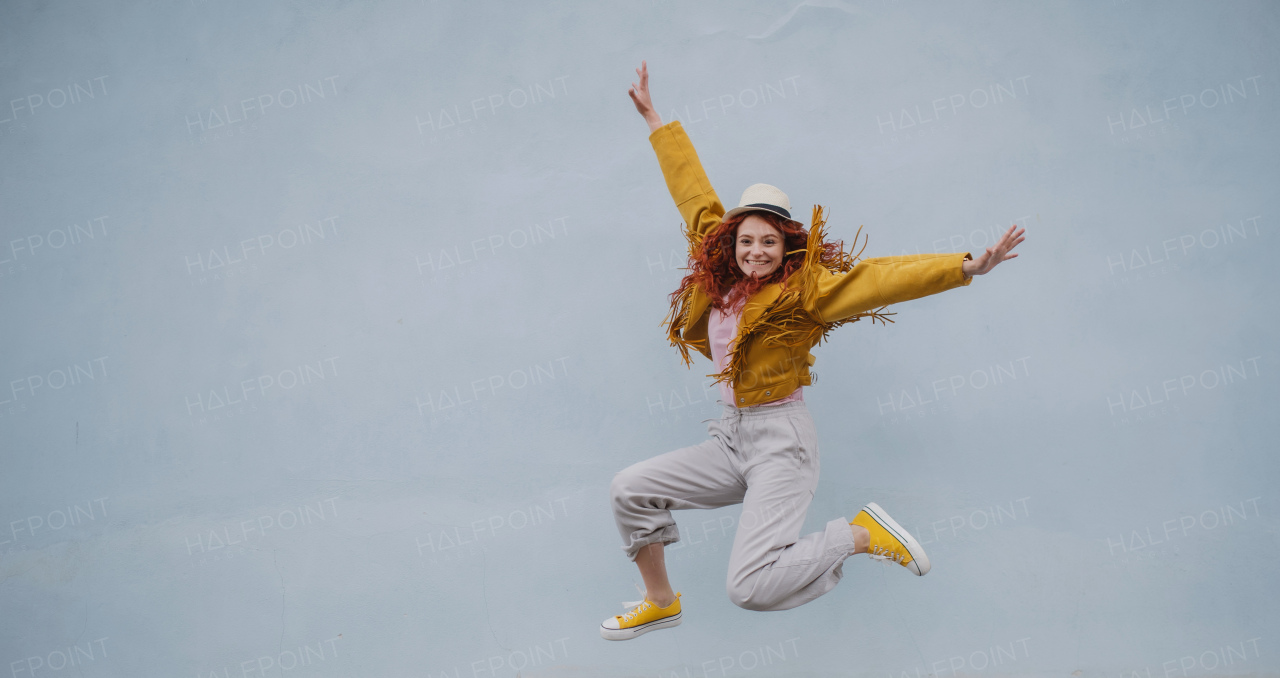 A cheerful young woman outdoors against white background, jumping.