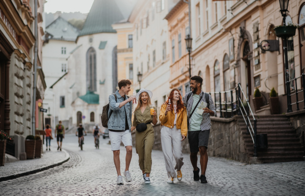 A front view of group of happy young people with drinks outdoors on street on town trip, laughing.