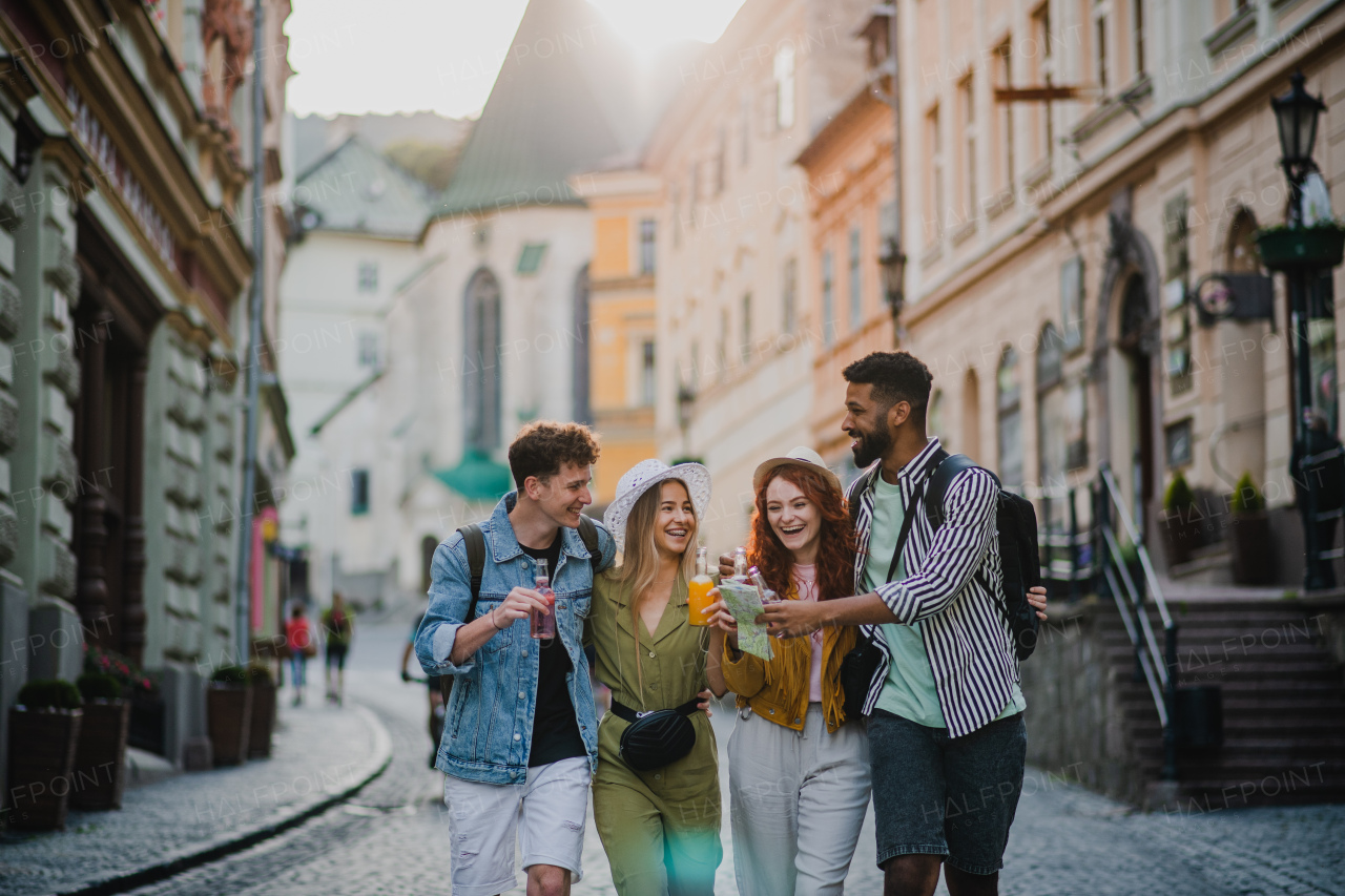 A front view of group of happy young people outdoors on street on town trip, walking with drinks.