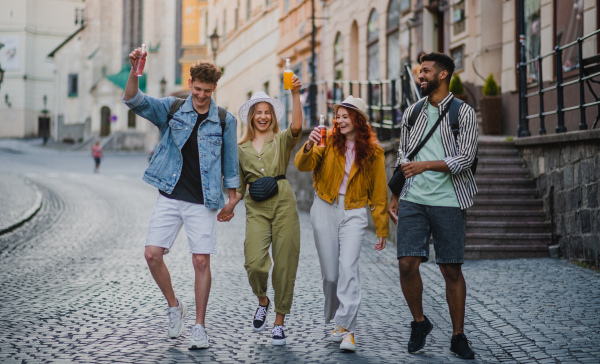 A front view of group of happy young people with drinks outdoors on street on town trip, laughing.