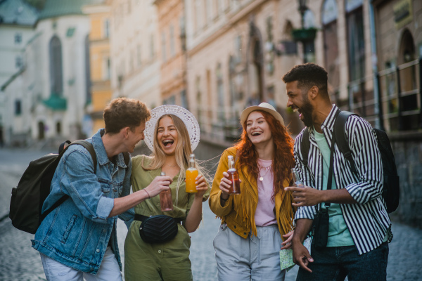 A front view of group of happy young people with drinks outdoors on street on town trip, laughing.