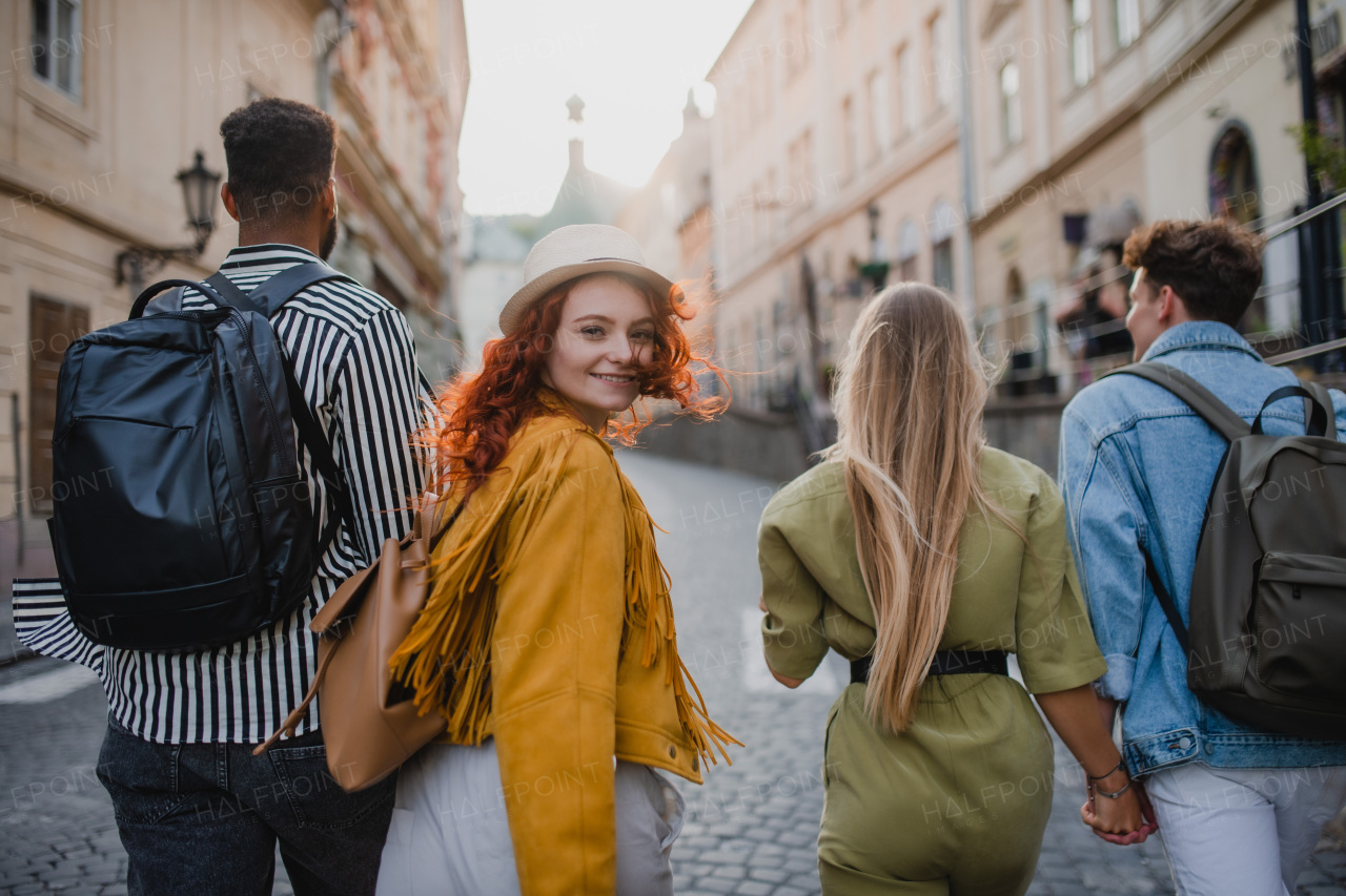 A rear view of group of happy young people outdoors on trip in town, walking and looking back.