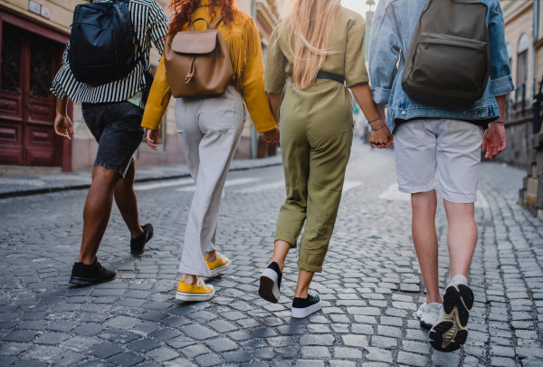 A rear view of group of young people outdoors on trip in town, walking and holding hands.