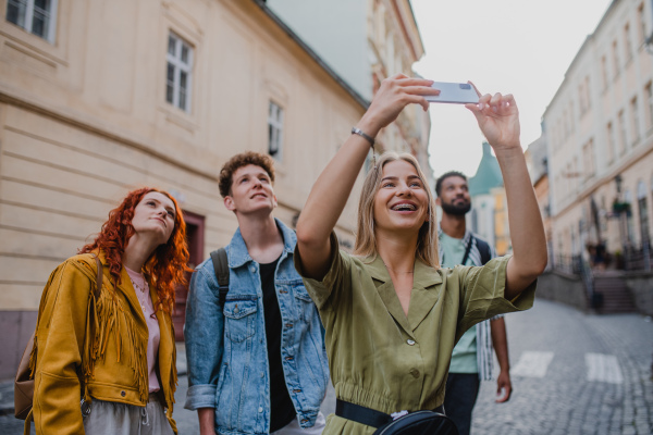 Group of young people tourists sightseeing outdoors on trip in town, taking photographs with smartphone.