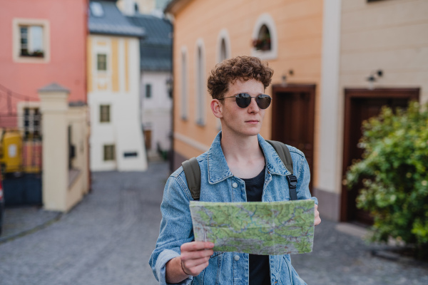 A happy young man tourist outdoors on trip in town, using map.