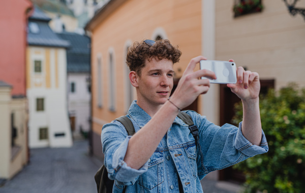 A young man outdoors on trip in town, taking photograph with smartphone.