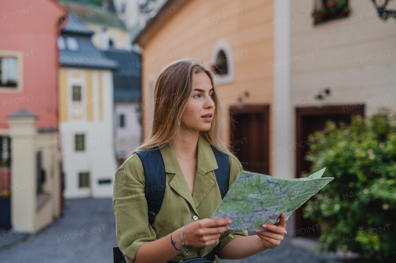 A happy young woman tourist outdoors on trip in town, using map.