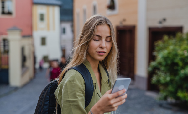 Happy young woman tourist outdoors on trip in town, taking selfie with smartphone.