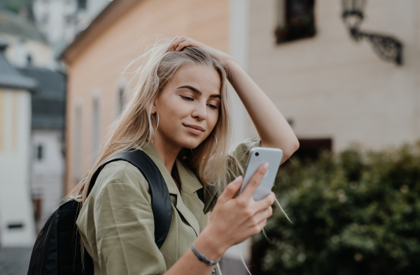 Happy young woman tourist outdoors on trip in town, taking selfie with smartphone.