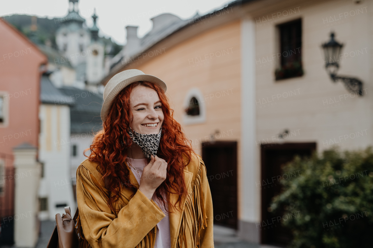 A young woman tourist with face mask outdoors on trip in town, looking at camera.