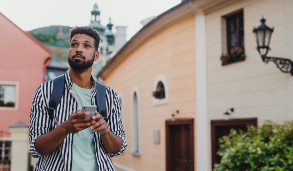 A young man outdoors on trip in town, using online map on smartphone.